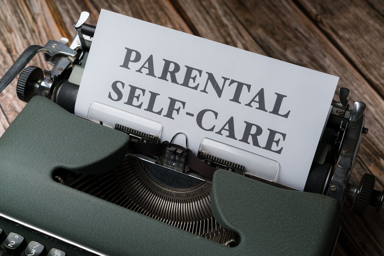 A vintage typewriter typing the phrase 'Parental Self-Care' on a wooden table.